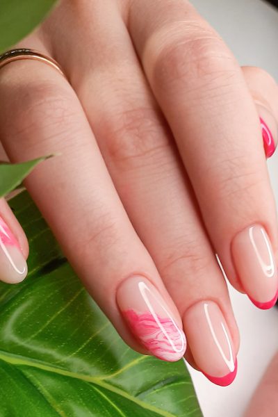 Beautiful pink French manicure with abstract design. Women's fingers with beautiful long nails on a background of green leaves