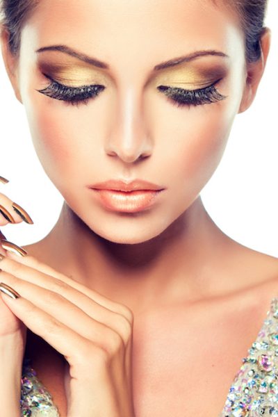 Golden make up, bright gilded manicure and elegant gesture. Close up portrait of attractive woman model.